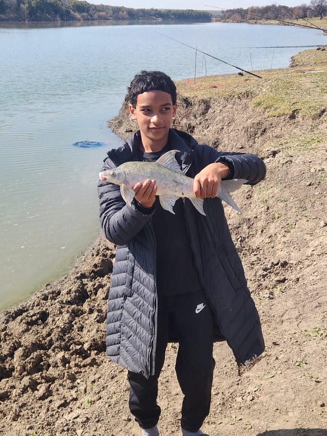 A young angler holding up a larger fish caught from the riverbank.